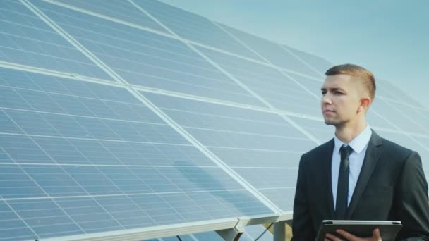 Empresario con una tableta en sus manos va a lo largo de una fila de paneles solares. Desarrollo de energías alternativas. Steadicam tiro — Vídeo de stock