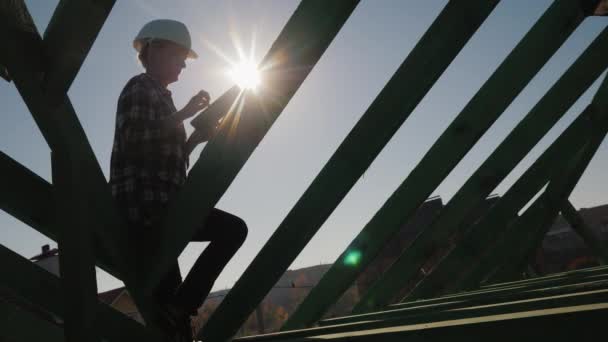 Silhouette d'un ingénieur, travaille parmi les chevrons du toit, utilise une tablette. Contrôle technique dans la construction — Video