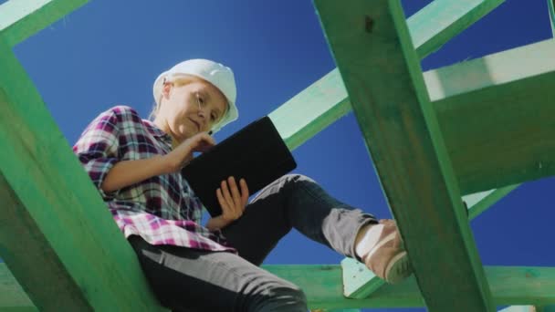 Vídeo de bajo ángulo: ingeniero, trabaja entre las vigas del techo, utiliza una tableta. Control técnico en la construcción — Vídeo de stock