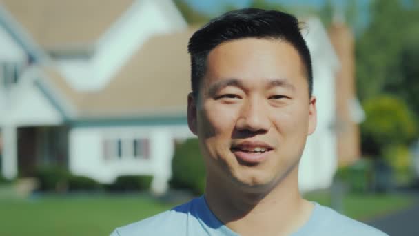 Porträtt av en ung asiatisk man. Leende tittar på kameran mot en suddig bakgrund på house. — Stockvideo