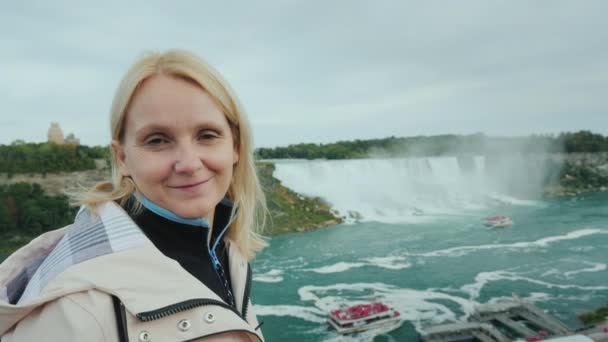 Ung Turist Står Mot Bakgrund Niagara Falls Ler Mot Kameran — Stockvideo