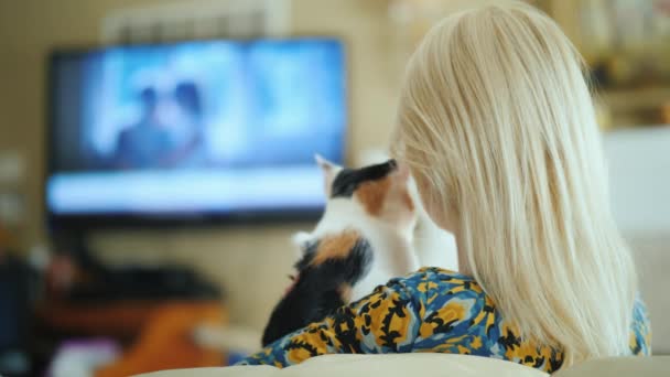 Szőke nő egy cica karjaiban tévénézés, hátsó nézet — Stock videók