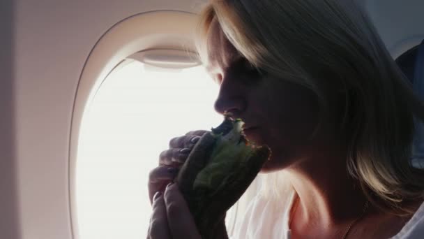 Silhouette einer Frau, die am Bullauge eines Flugzeugs ein Sandwich isst. — Stockvideo