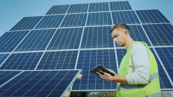 Un trabajador usa una tableta en un gran panel solar terrestre. energía alternativa — Foto de Stock