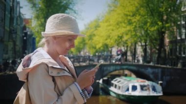 Çekici bir kadın Amsterdam'da güzel ve sakin kanallardan biri yakınındaki bir akıllı telefon kullanır. Hollanda Turizm