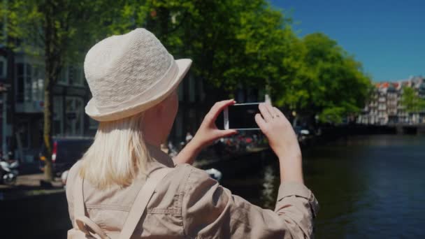 Χρησιμοποιώντας ένα smartphone, μια γυναίκα παίρνει μια όμορφη θέα το κανάλι του Άμστερνταμ. Ταξιδεύοντας στην Ολλανδία έννοια — Αρχείο Βίντεο