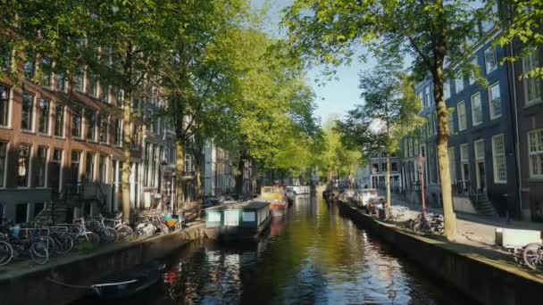 Schöne orte in amsterdam - ein gemütlicher kanal mit bargen, traditionellen fahrrädern vor der küste geparkt — Stockvideo