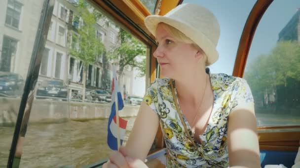 Una donna naviga su una nave da crociera attraverso i canali di Amsterdam. Detiene la bandiera dei Paesi Bassi. Concetto Turismo in Europa — Video Stock