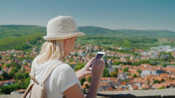 Mujer turista utiliza un teléfono inteligente en el fondo de la antigua hermosa ciudad europea. Casas con tejados de teja roja. Concepto de comunicación de viajes y vacaciones — Vídeo de stock