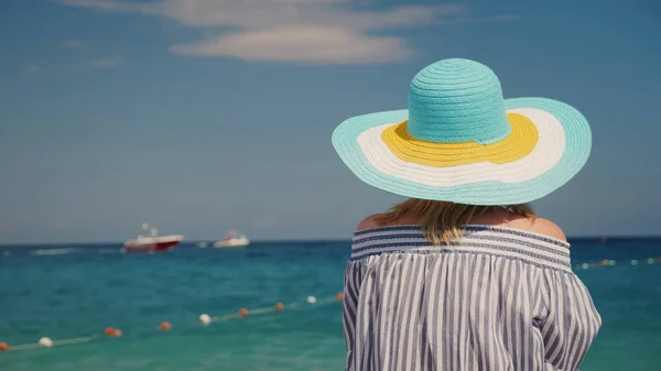 Uma mulher de chapéu admira o mar, uma vista traseira. Mulher em férias conceito — Fotografia de Stock