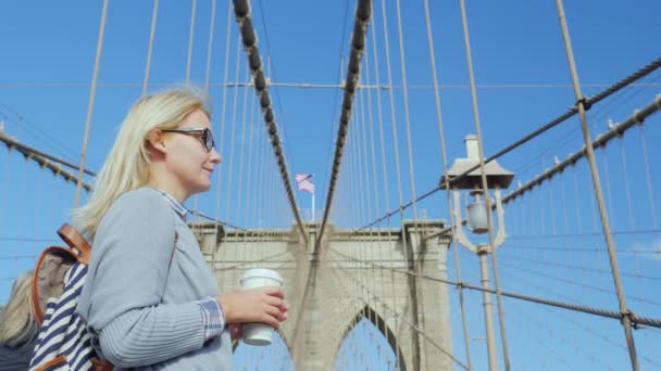 Uma jovem bebe café na Brooklyn Bridge, em Nova Iorque. Viagem e o início de um novo dia — Vídeo de Stock