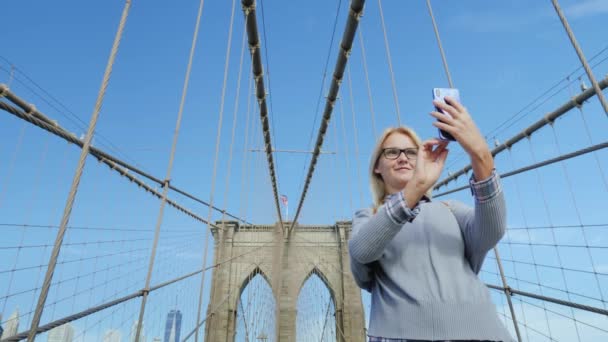 Женщина фотографирует себя на знаменитом Бруклинском мосту - одной из главных достопримечательностей Нью-Йорка — стоковое видео
