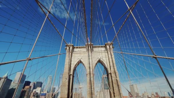 Vista en primera persona del puente de Brooklyn en dirección a Manhattan. Visto hermosos pilares del puente con cuerdas y la famosa silueta de rascacielos — Vídeos de Stock