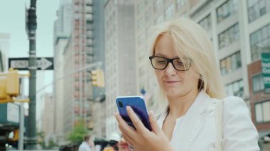 Genç bir kadın Manhattan şehir merkezindeki ofis binalarına karşı akıllı telefon kullanıyor. New York İş Konsepti