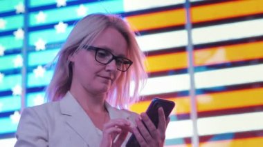 Times Meydanı'nda yeni Ylok içinde Amerikan bayrağı şeklinde parlayan bir tahta arka plan üzerinde bir smartphone genç turist kullanır