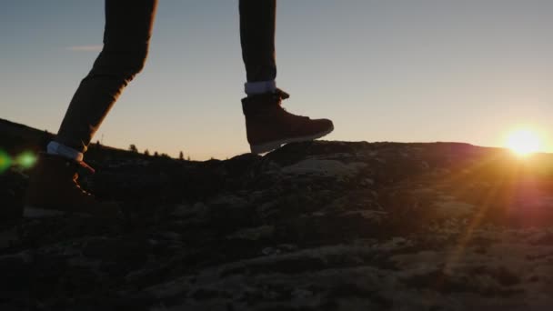 Una mujer en botas de trekking camina por las piedras, el sol naciente ilumina maravillosamente las piernas — Vídeos de Stock