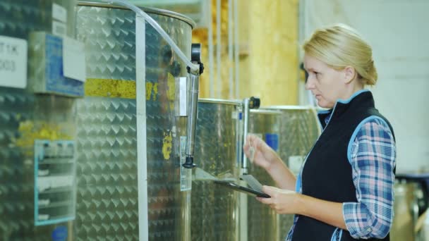 Eine Frau mit Tablette arbeitet in der Nähe des Futtertanks, kontrolliert das Etikett auf der Tonne. Qualitätskontrolle in der Lebensmittelproduktion — Stockvideo