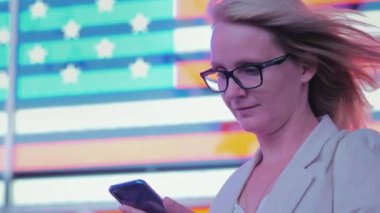İş kadını New York'ta ünlü Times Meydanı nda büyük bir Amerikan bayrağı arka plan üzerinde bir akıllı telefon kullanır. İş ABD kavram