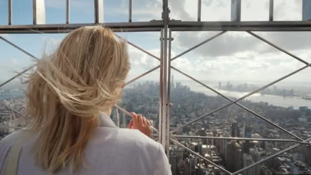 The woman looks at the metropolis below. It stands at the fence, rear view. In the distance, visible skyscrapers of New York — Stock Video