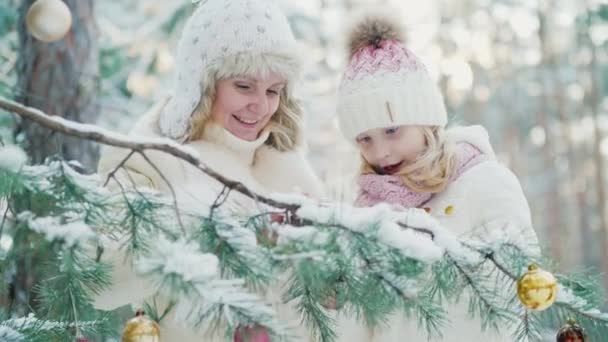 In previsione del Natale, mamma e una bambina decorano nel cortile della casa un albero di Natale con palline giocattolo. — Video Stock