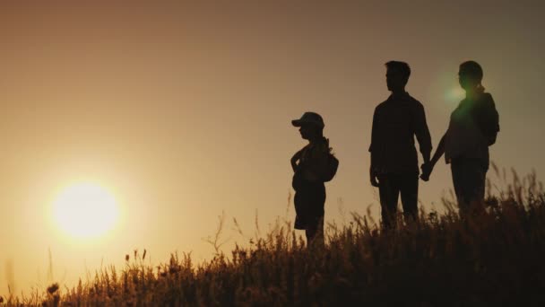 Счастливая семья с одним ребенком. Встаньте бок о бок на холме, любуясь закатом — стоковое видео