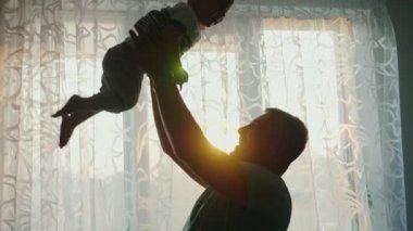 Siluetleri evlerinin pencereden bir çocukla ebeveyn sevgi dolu. Baba bebek oğlu ile oynar, annem onun yanında duruyor. Mutlu bir aile