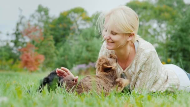 Heureux avec vos chiots préférés. Une femme joue avec deux chiens, allongée sur une pelouse dans sa cour — Video