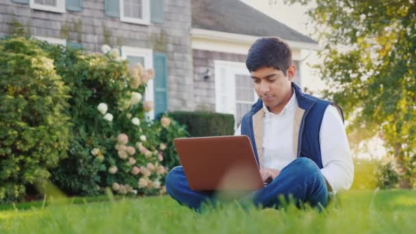 Un joven de nacionalidad india disfruta de un portátil en su patio trasero — Vídeo de stock