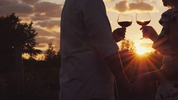 Романтична пара тримає руки клінт окуляри з вином на заході сонця . — стокове фото