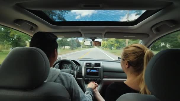 Romántica pareja multiétnica montando en el coche, tomados de la mano. Están iluminados por la luz de la escotilla de los coches . — Vídeo de stock