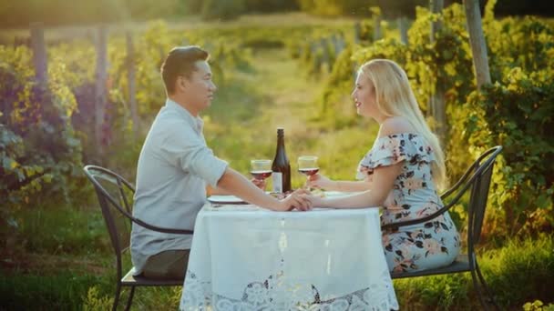 Una joven pareja multiétnica está cenando con copas de vino en un pintoresco lugar cerca del viñedo. Antes del atardecer — Vídeo de stock