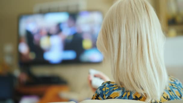 背面: 女性は居間でテレビを見ています。リモート コントロールを保持します — ストック動画