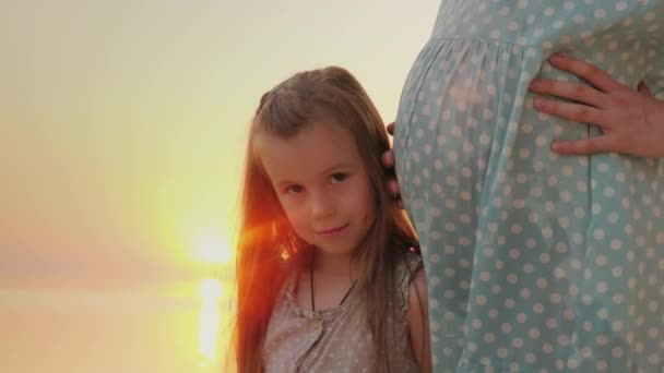 Retrato de un niño feliz cerca de una madre embarazada. Contra el fondo de la puesta de sol sobre el mar — Vídeos de Stock