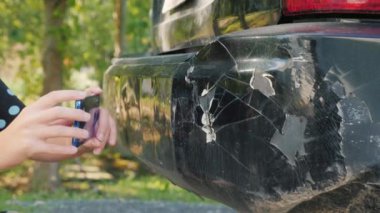 Bir kadın hasarlı bir araba tamponunun fotoğrafını çekiyor.