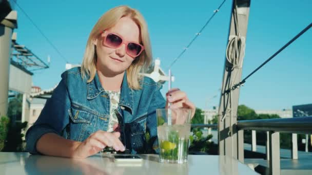 Una mujer utiliza un teléfono inteligente, descansando en un café de verano. Conexión en concepto de vacaciones — Vídeo de stock