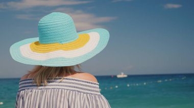 Şapkalı bir kadın masmavi deniz görünüyor. Rüya tatil kavramı