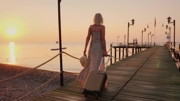Een vrouw in een ontwikkelende jurk is haast rechtstreeks vanuit het vliegtuig naar de pier van de zee om te genieten van rust en stilte in de vroege ochtend — Stockvideo