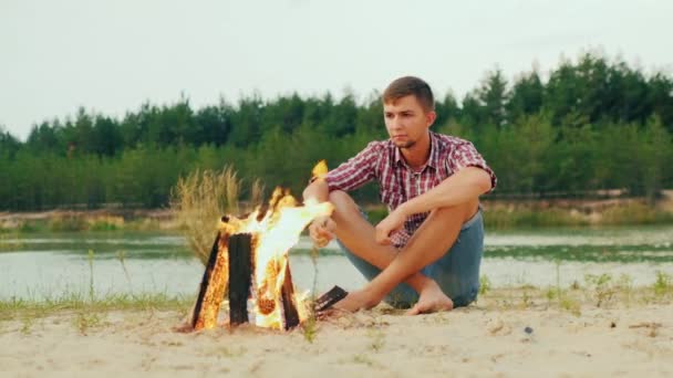 Uomo serio e solitario seduto vicino al falò, arrosto di marshmallow su un bastone — Video Stock