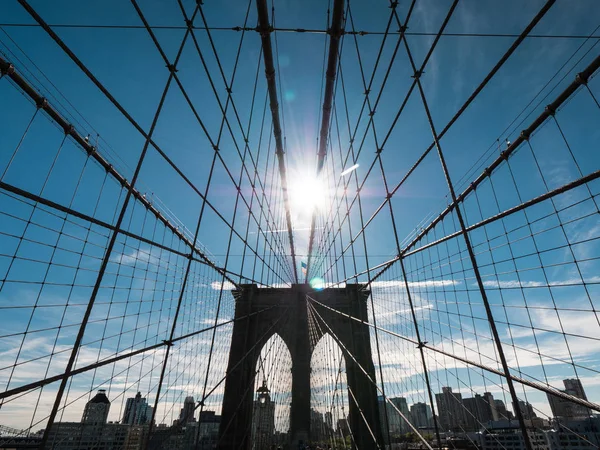 La silueta del famoso puente de Brooklyn, el sol en su cenit brilla sobre sus pilares. Uno de los símbolos más famosos de Nueva York — Foto de Stock