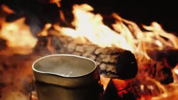 In een klein kampvuur in de buurt van het vuur kookt water — Stockvideo