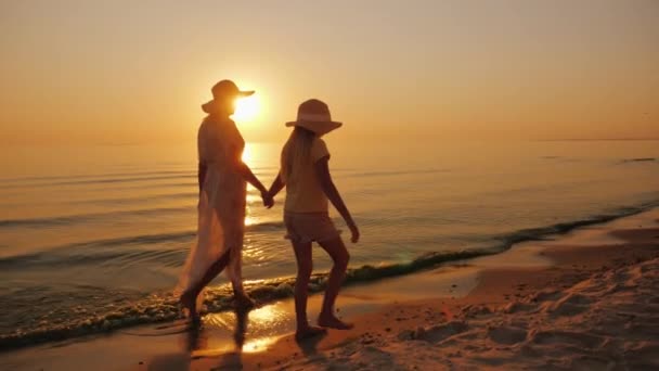 Uma mulher e sua filha caminham juntas ao longo da areia na praia . — Vídeo de Stock