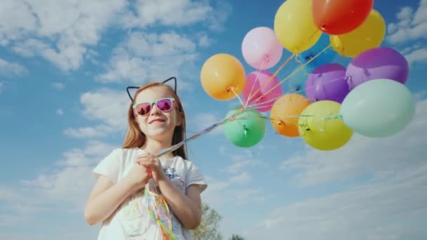 Una chica alegre en gafas de sol con orejas de gatos sosteniendo globos — Vídeos de Stock