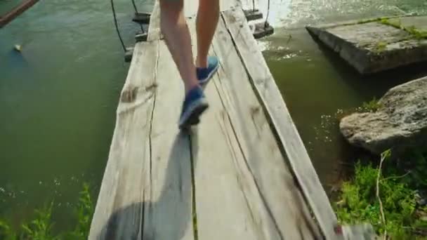 Męskie nogi iść wzdłuż wąskich drewniany most nad przepaścią i górskiej rzece. Przezwyciężyć strach przed pojęcia — Wideo stockowe