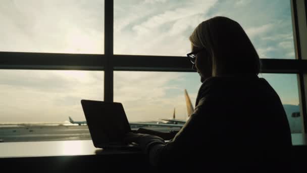 Біля великого вікна аеропорту сидить жінка з ноутбуком. Завжди на зв'язку, концепція ділової жінки — стокове відео