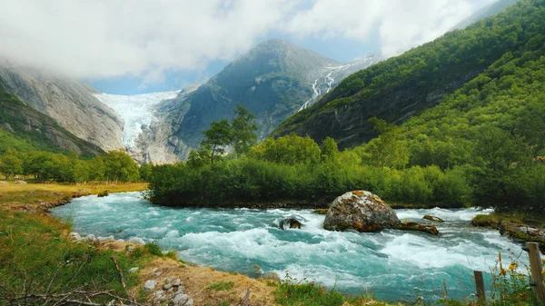 Lente larga: Glaciar Briksdal com um rio de montanha em primeiro plano. A natureza incrível da Noruega — Fotografia de Stock