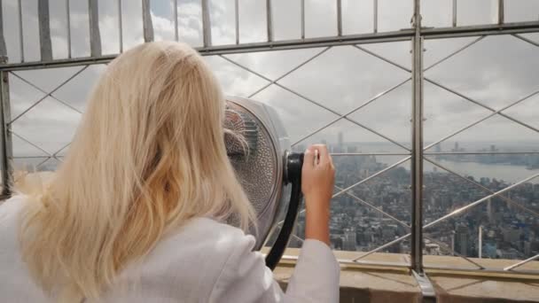 Vista posterior: Mujer rubia mirando a través de prismáticos en el panorama de Nueva York. Visita el concepto de Nueva York — Vídeos de Stock