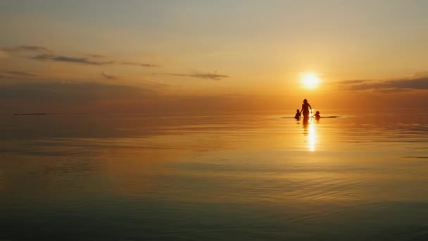 Matka s dvěma dětmi smát v moři při západu slunce — Stock video