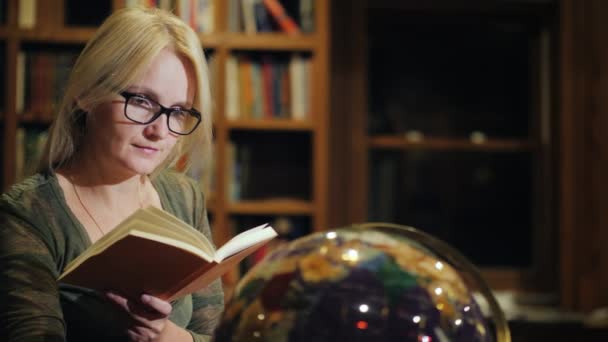 Woman with a book in hand looks at the globe — Stock Video