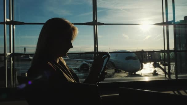 Silueta ženy podnikání pomocí smartphone poblíž velké okno v letištním terminálu — Stock video