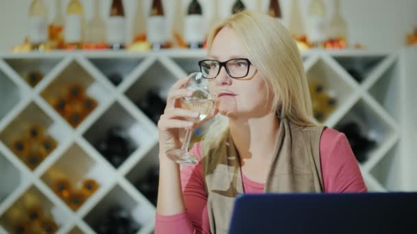 Degustación de vinos en una acogedora bodega. Mujer con un vaso se sienta cerca de la computadora portátil — Vídeos de Stock